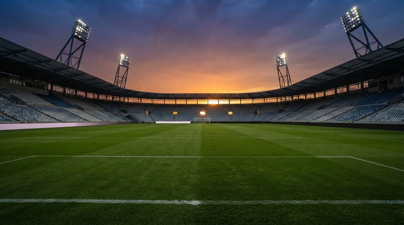 Un estadio de fútbol vacío con torres de iluminación al atardecer